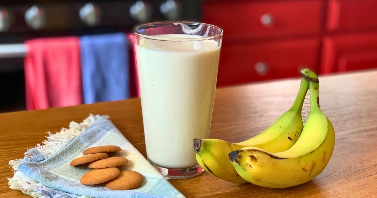 Banana cream pie smoothie in a glass beside a whole banana and a stack of vanilla wafers.