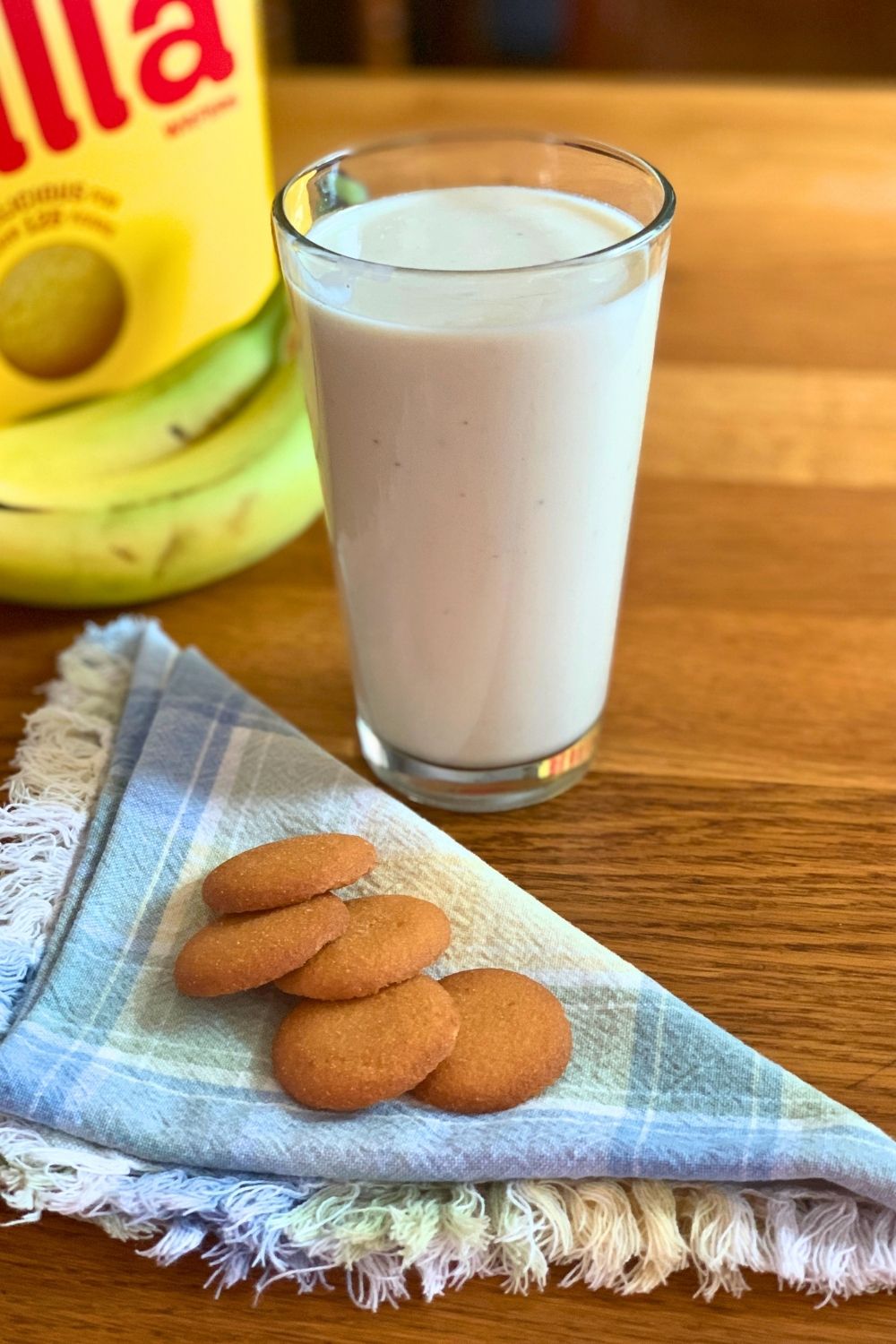 A glass full of a warm white smoothie beside a handful of vanilla wafers.