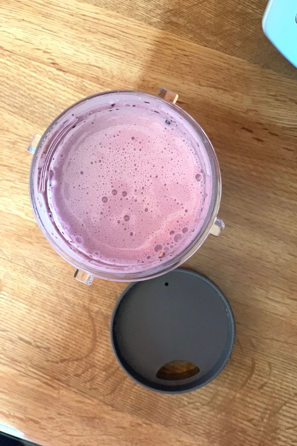 Overhead view of a pale purple smoothie in a cup beside a lid.