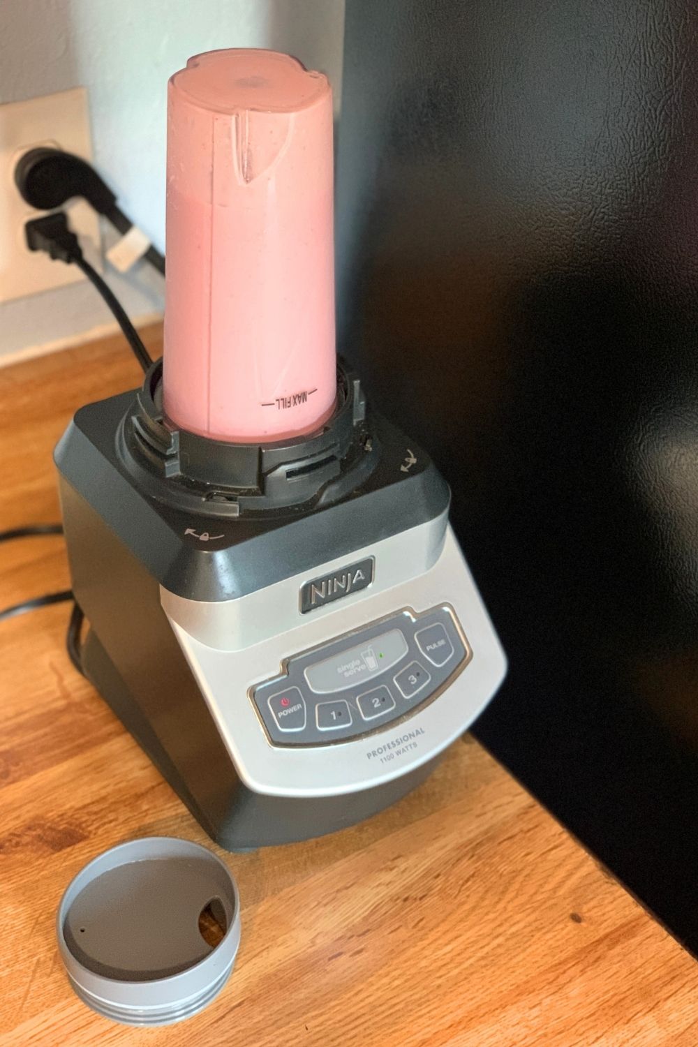 A blender with a plastic cup filled with a pink mixture.