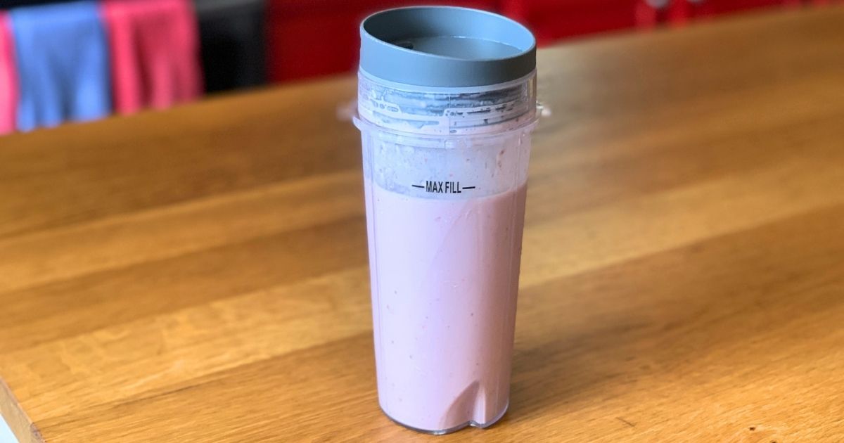A pink cherry pie smoothie in a plastic blender cup with a lid.