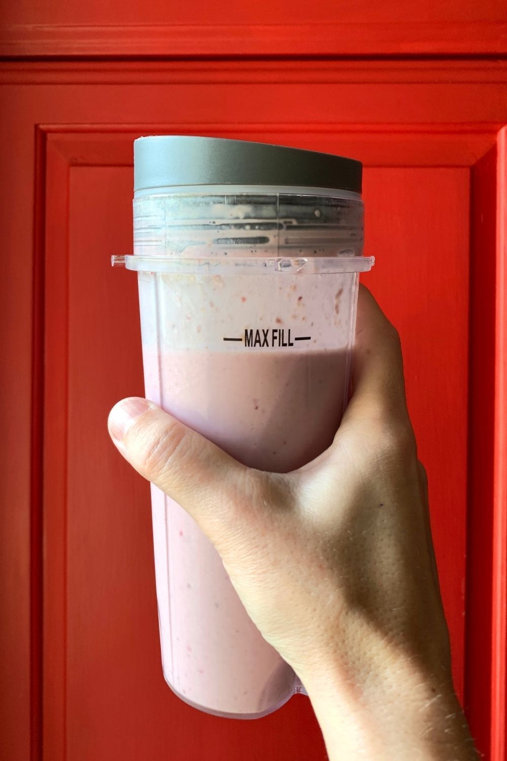 A hand holding a pink cherry pie smoothie in a plastic blender cup.