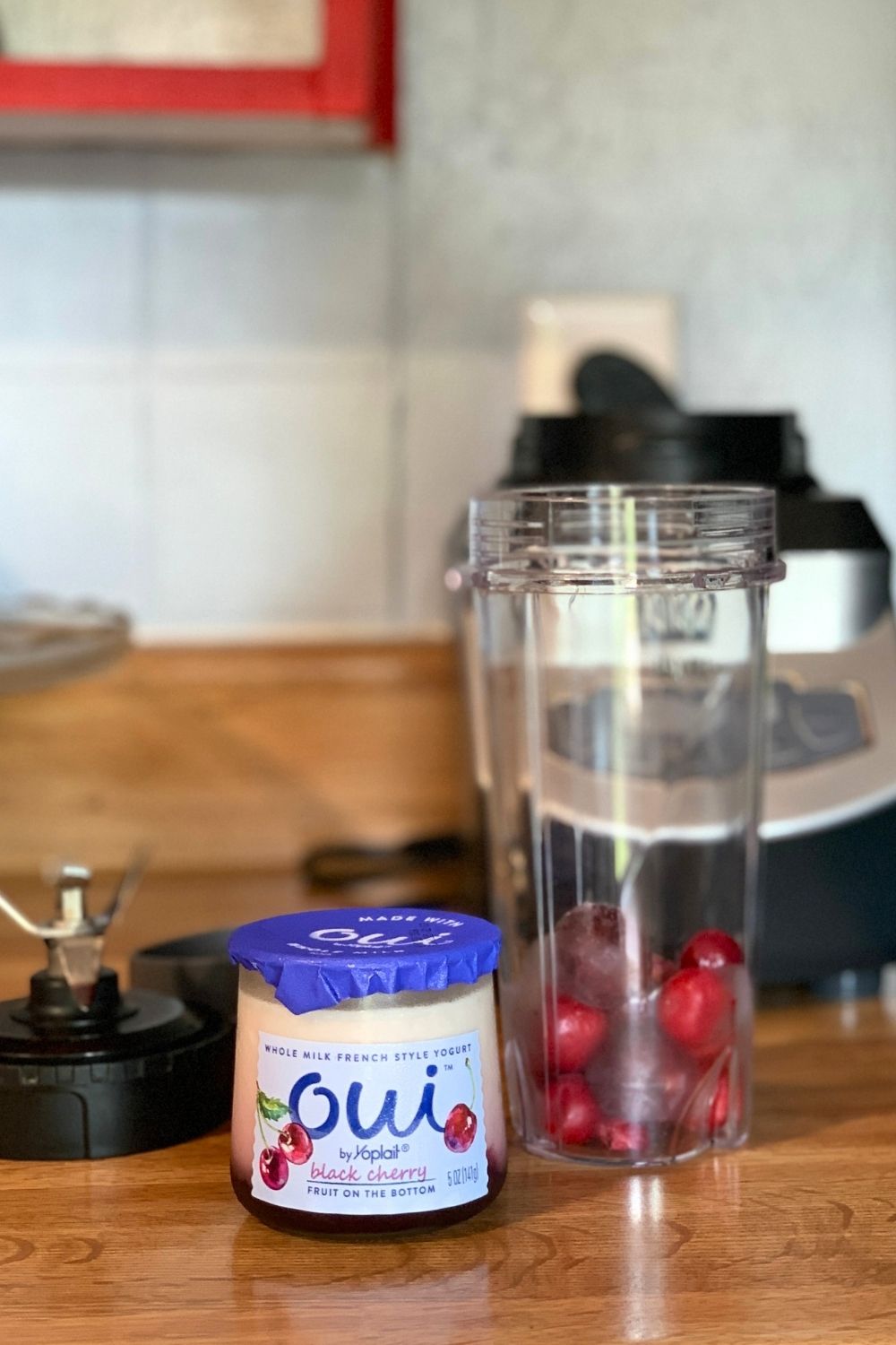 A glass jar of Oui black cherry yogurt beside a cup of frozen cherries.