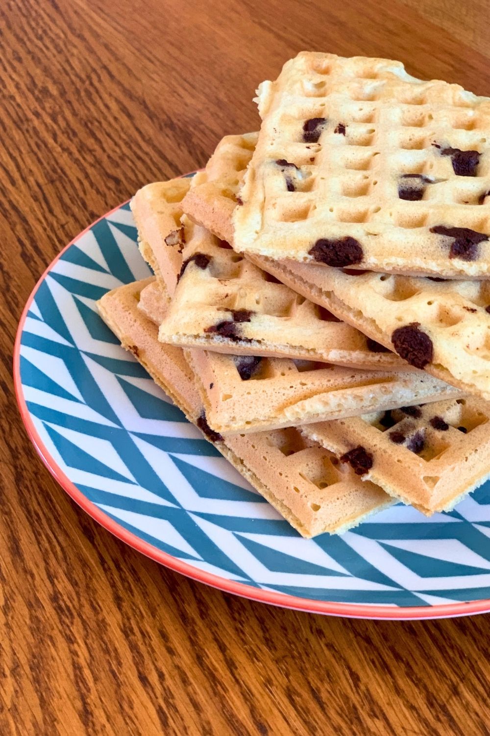 A plate stacked with golden yellow-brown waffles with chocolate chips.