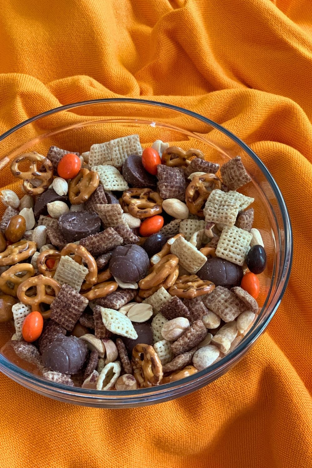 Closeup of a bowl of chocolate Chex cereal, mini pretzels, pumpkin pie M&Ms, roasted peanuts, and Reese's mini peanut butter cups.