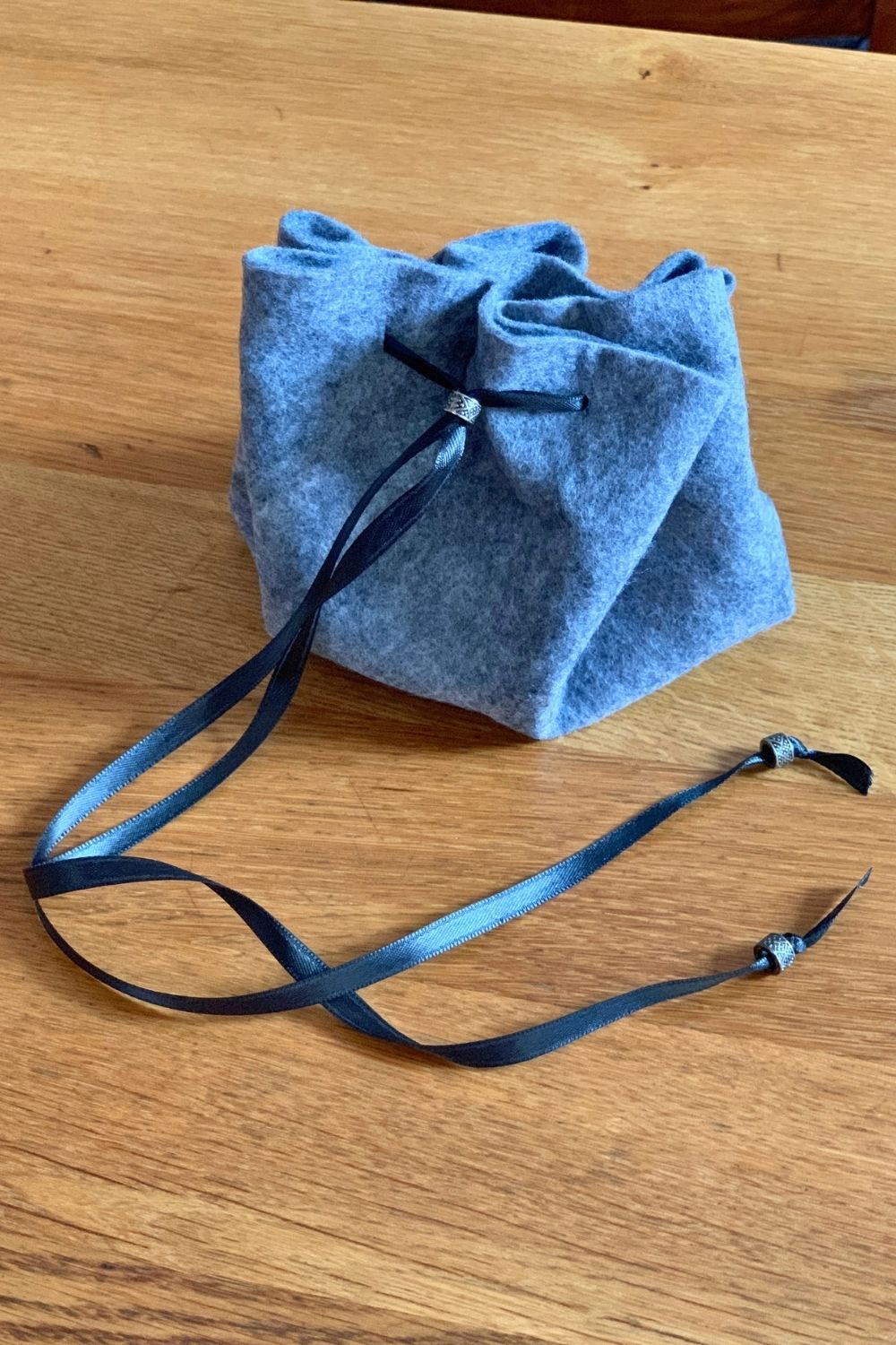 A drawstring no-sew dice bag made from gray felt and black ribbon.