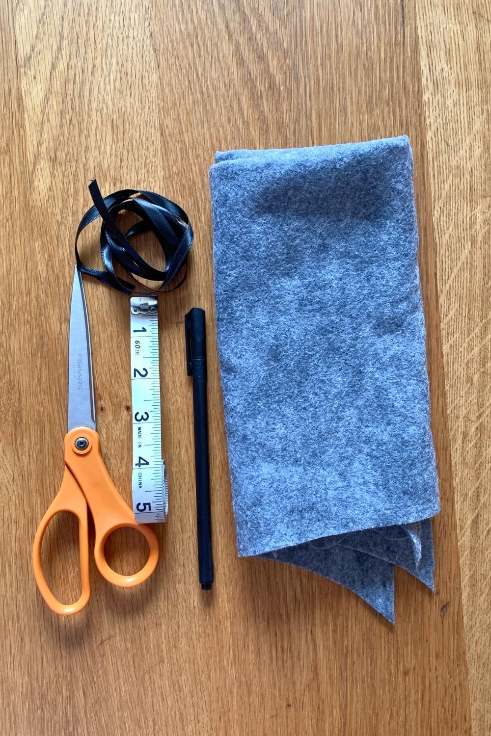 A pair of scissors, a black ribbon, pen, fabric tape measure, and piece of gray felt.