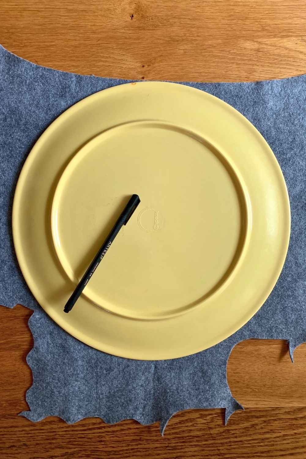 A large yellow plate on top of a piece of gray felt with a pen to trace the outline.