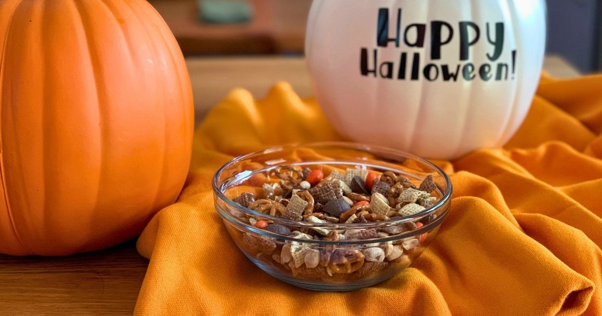 A bowl of Halloween snack mix made with chocolate Chex cereal, pretzels, M&Ms, peanuts, and mini peanut butter cups.
