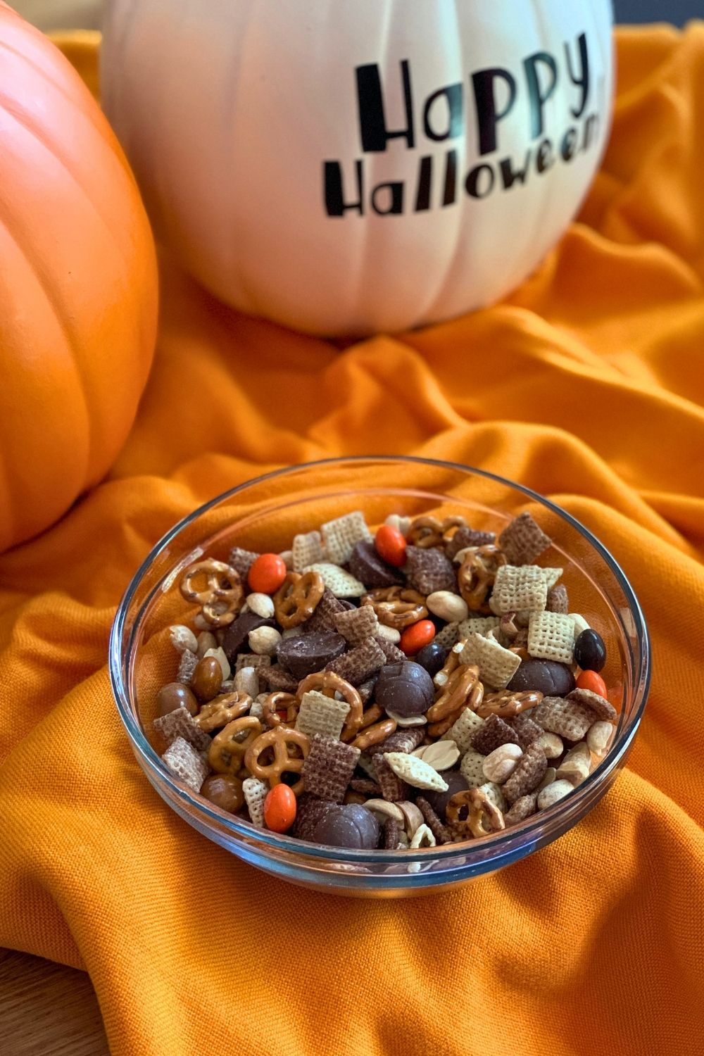 A bowl of Halloween snack mix made with chocolate Chex cereal, pretzels, M&Ms, peanuts, and mini peanut butter cups.