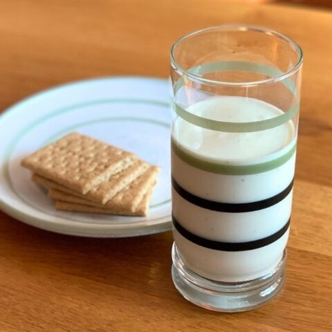 A pale yellow-green key lime pie smoothie in a striped glass beside a plate of graham crackers.