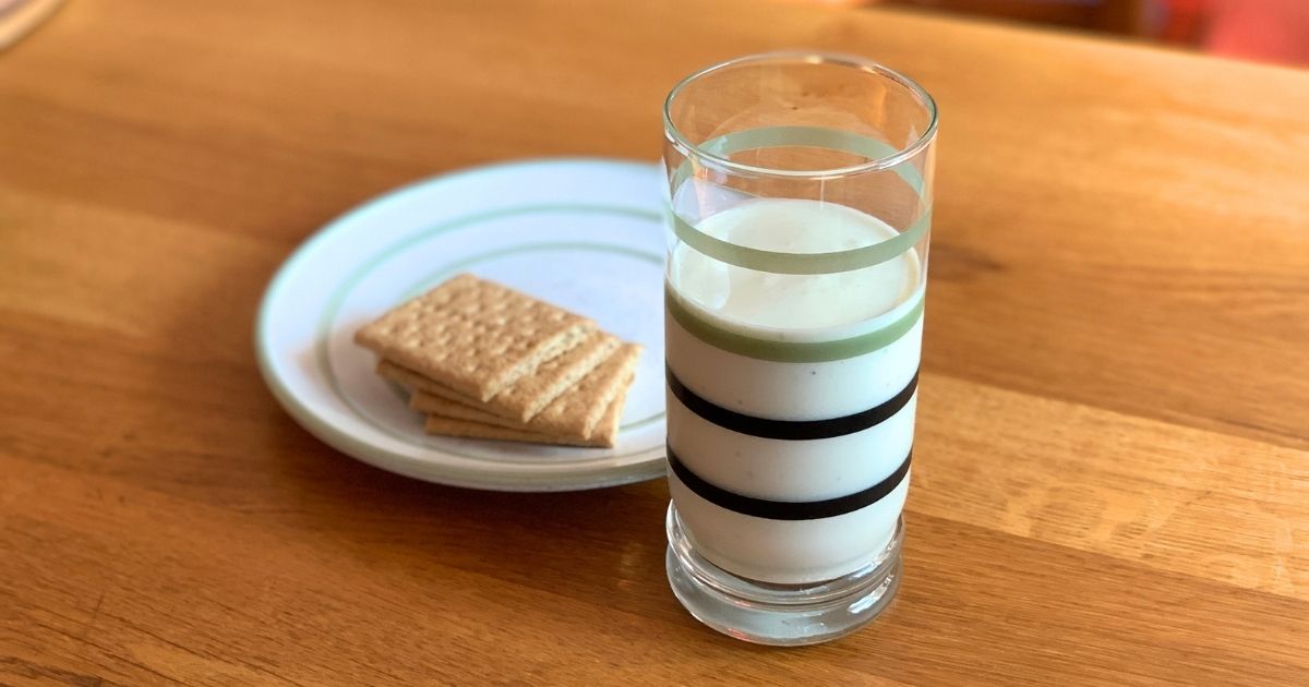 A pale yellow-green key lime pie smoothie in a striped glass beside a plate of graham crackers.