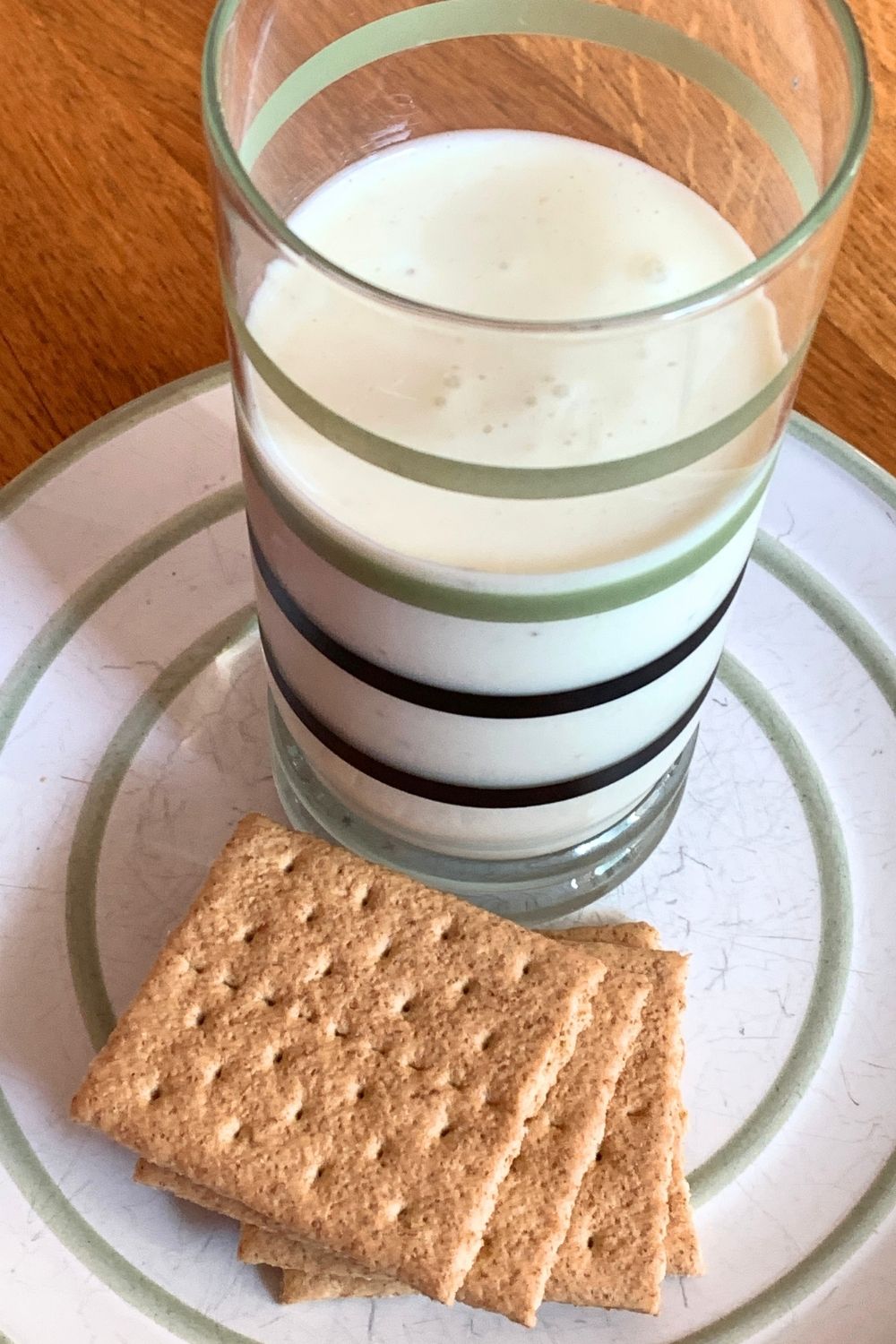 A pale yellow-green key lime pie smoothie in a striped glass beside a plate of graham crackers.