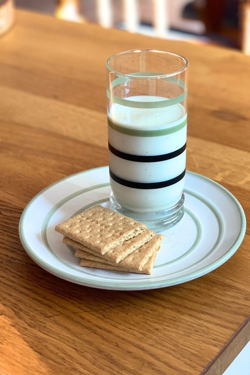 A pale yellow-green key lime pie smoothie in a striped glass beside a plate of graham crackers.