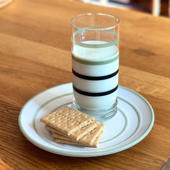 A glass of key lime pie smoothie on a plate beside graham cracker squares.