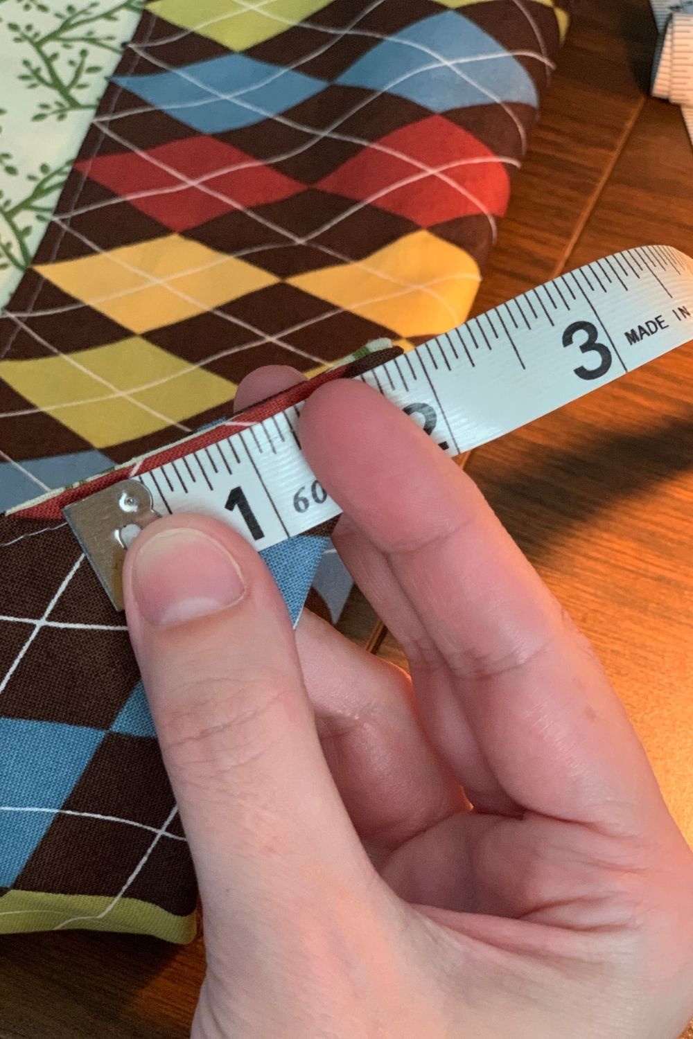 Holding a tape measure to mark 2 inches from a folded corner of fabric.