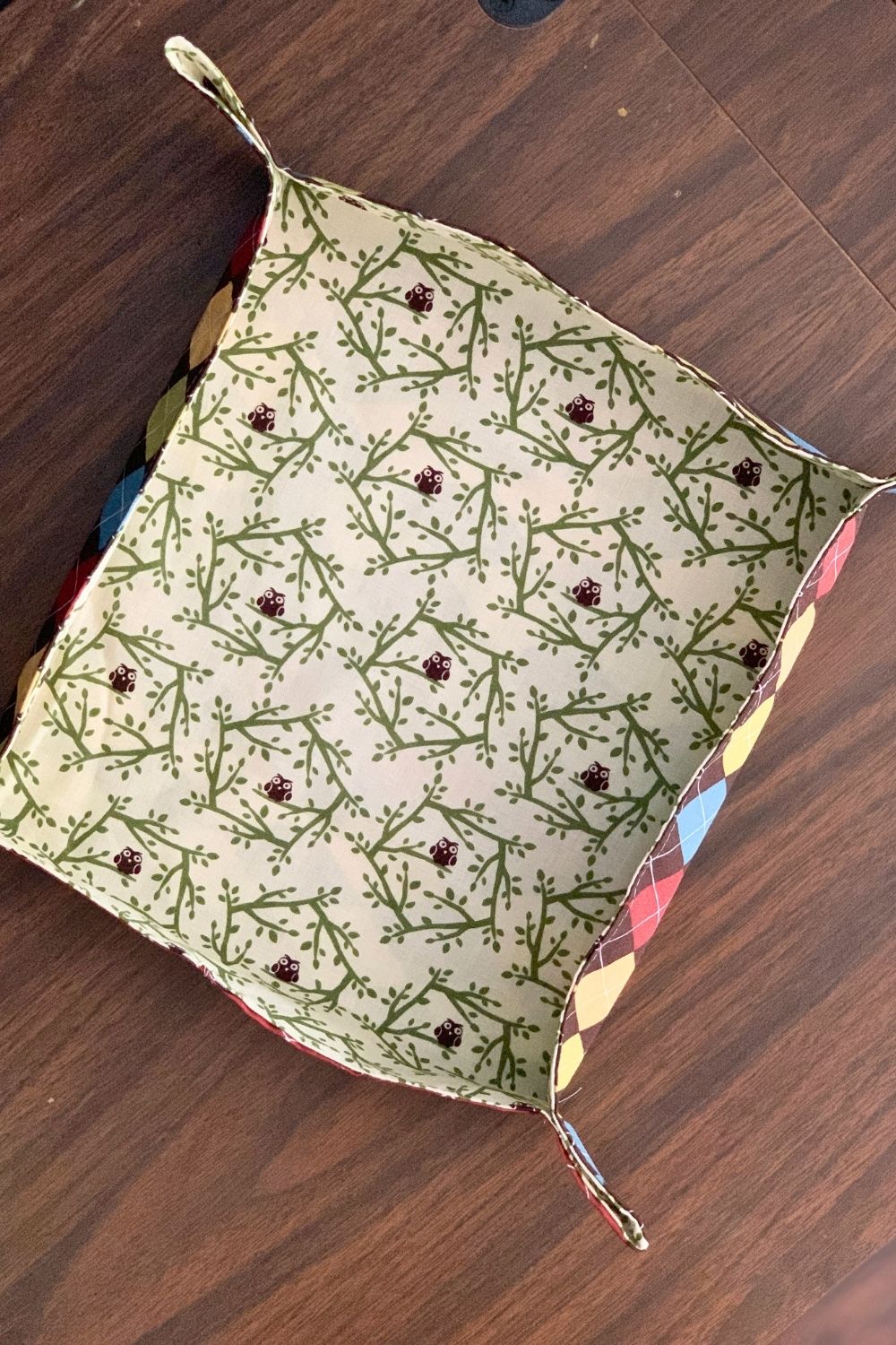 Overhead view of a finished fabric tray in contrasting patterns with a square shape and stitched triangular corners.