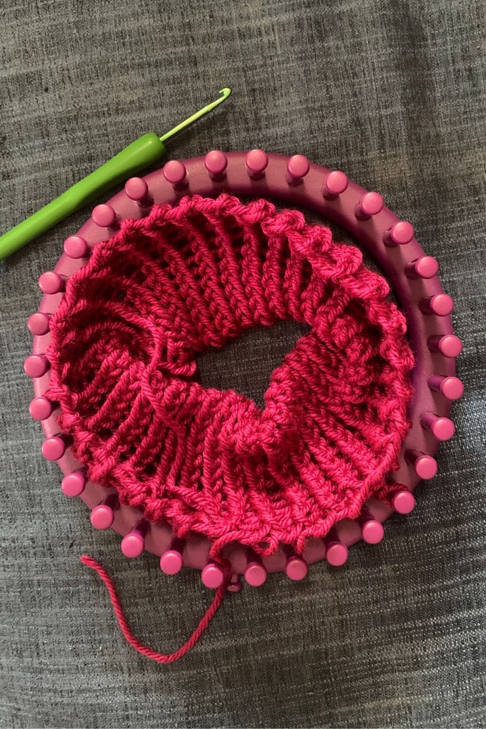 A knitted headband removed from a loom with a single dropped loop still on the loom at the bottom right.