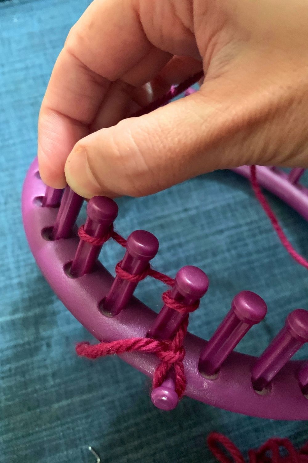 E-wrapping yarn around the pegs of a round knitting loom.