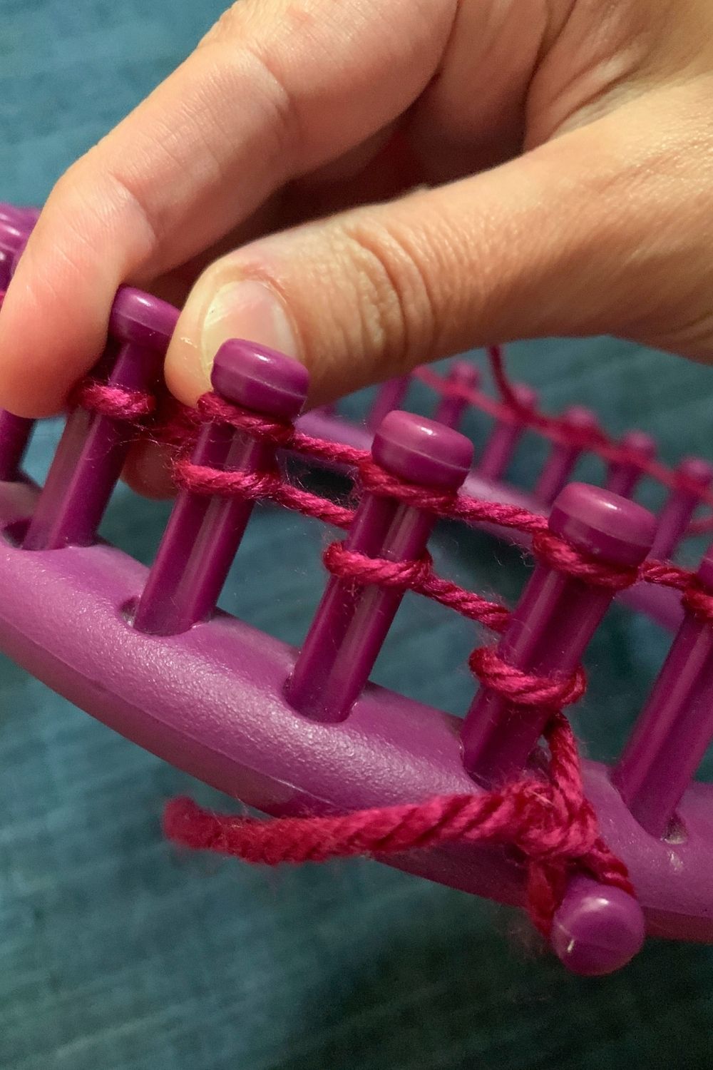 Wrapping a second row of yarn around the pegs of a loom.