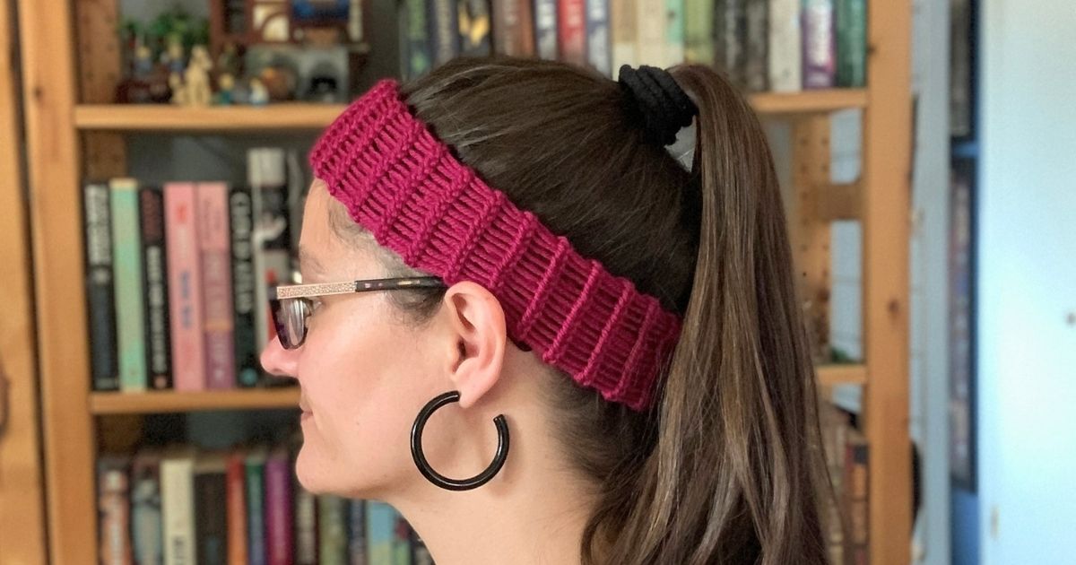 A woman with long hair up in a ponytail wearing a purple loom knit headband.