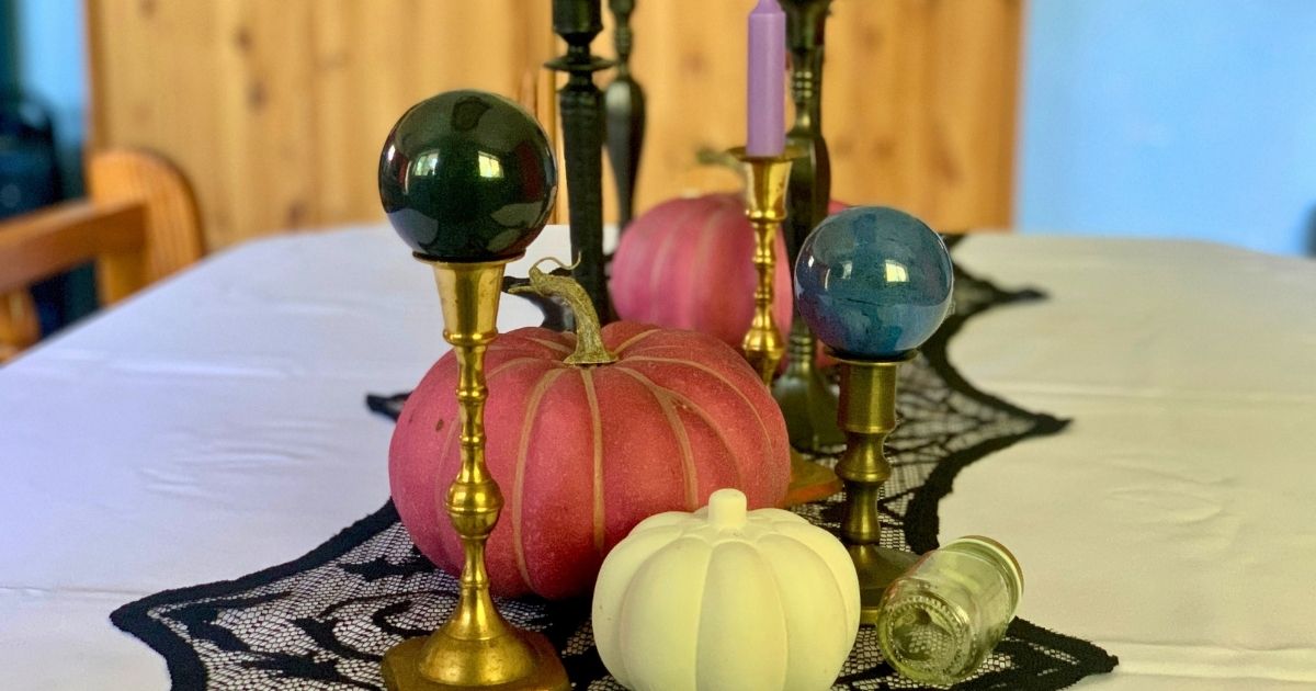 Tablescape of brass candlesticks, pink and white pumpkins, and painted ball ornaments displayed as gazing orbs.