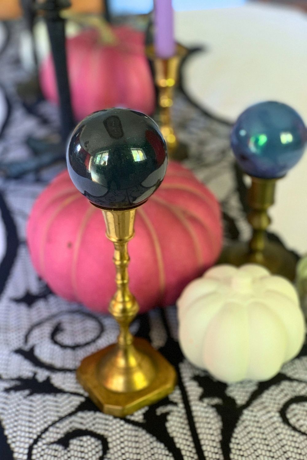 Black and blue glittery ball ornaments balanced on top of brass candlestick holders.