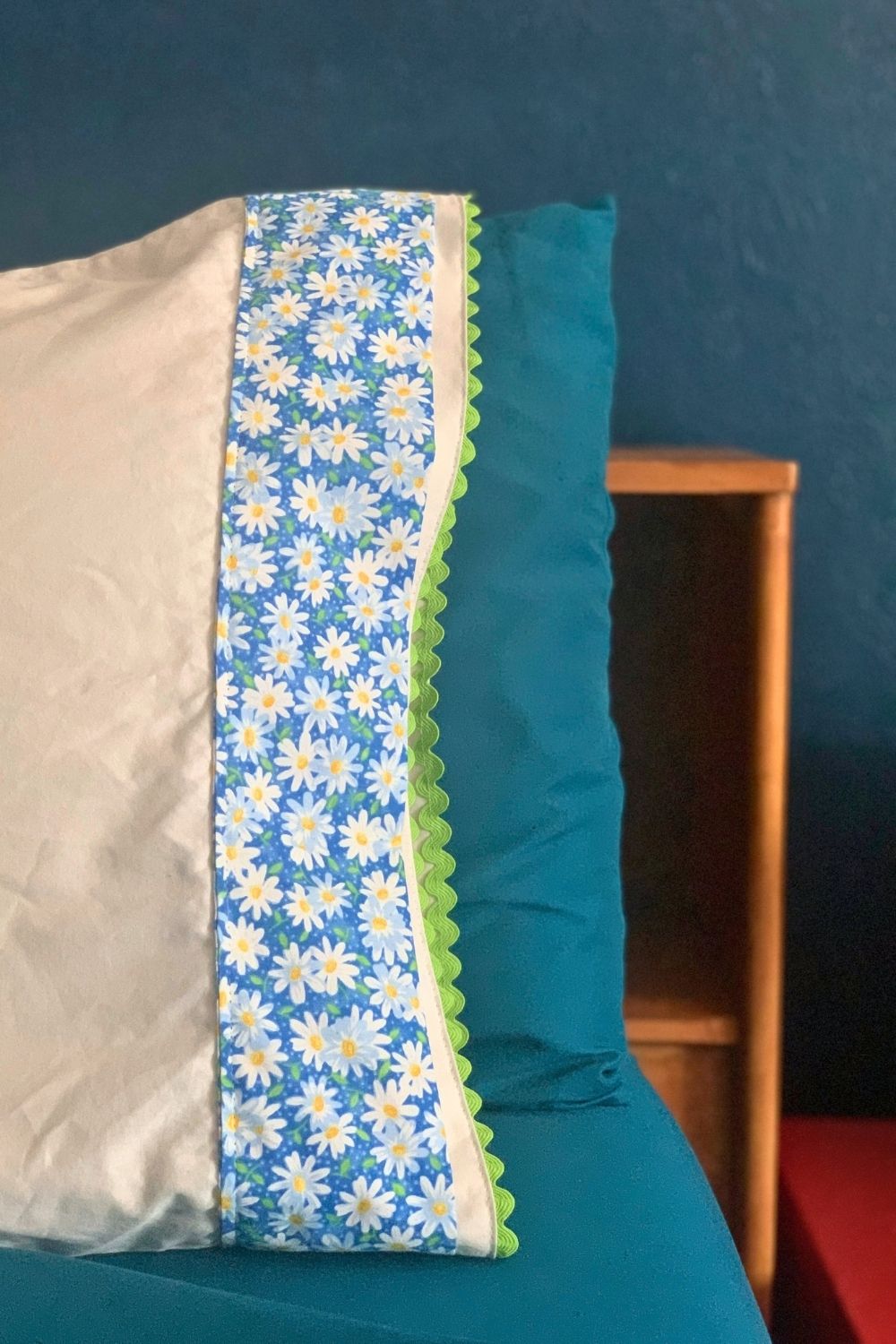 A white bed pillow case with blue and white daisy fabric and green rick rack added to the edge.