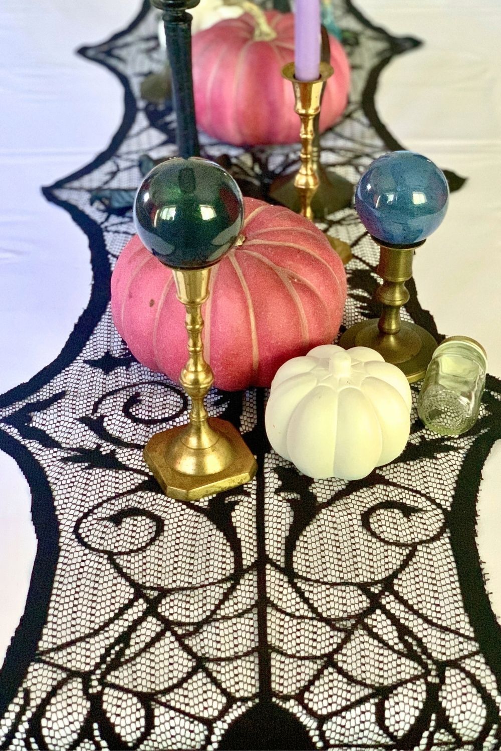 Tablescape of brass candlesticks, pink and white pumpkins, and painted ball ornaments displayed as gazing orbs.