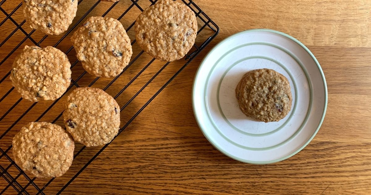 Oatmeal craisin cookies stacked on a plate beside a cooling rack filled with more cookies.