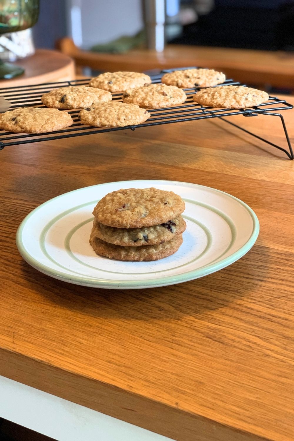 A stack of cranberry oatmeal cookies on a plate in front of a wire rack filled with more cookies.