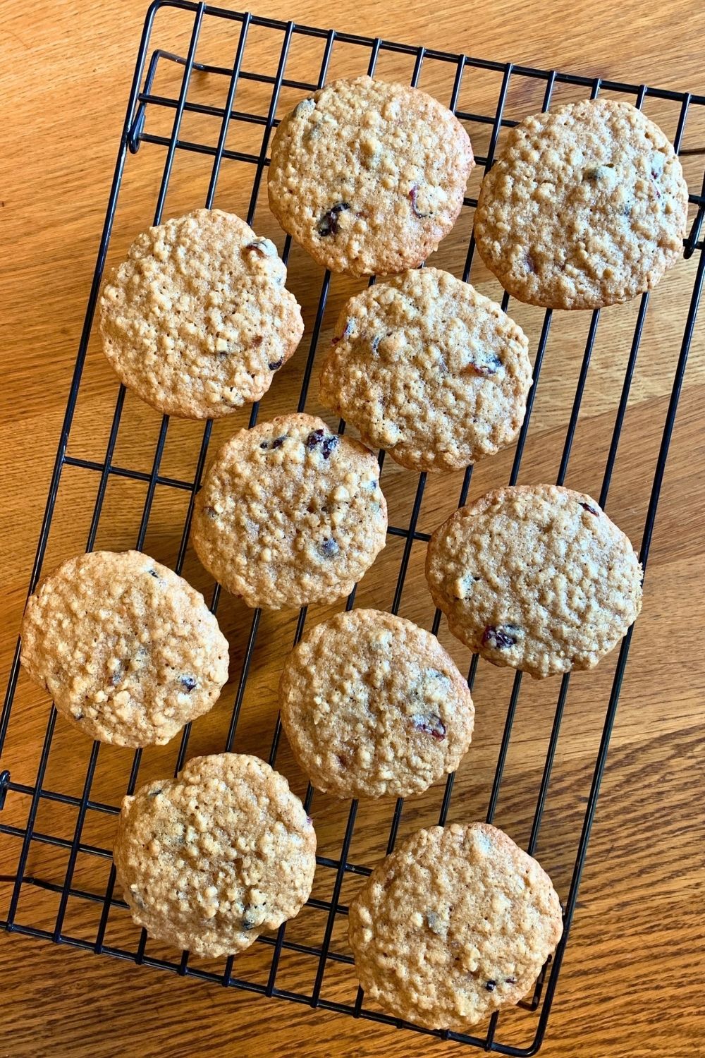 Oatmeal craisin cookies stacked on a plate beside a cooling rack filled with more cookies.