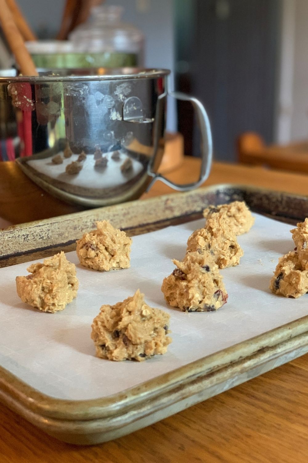 A baking sheet lined with parchment holding 8 blobby oatmeal craisin cookie dough balls.