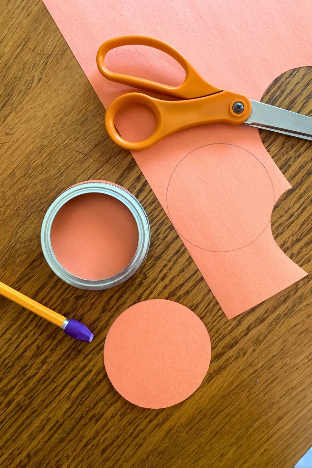 A pair of scissors and cut paper beside 2 orange paper circles.