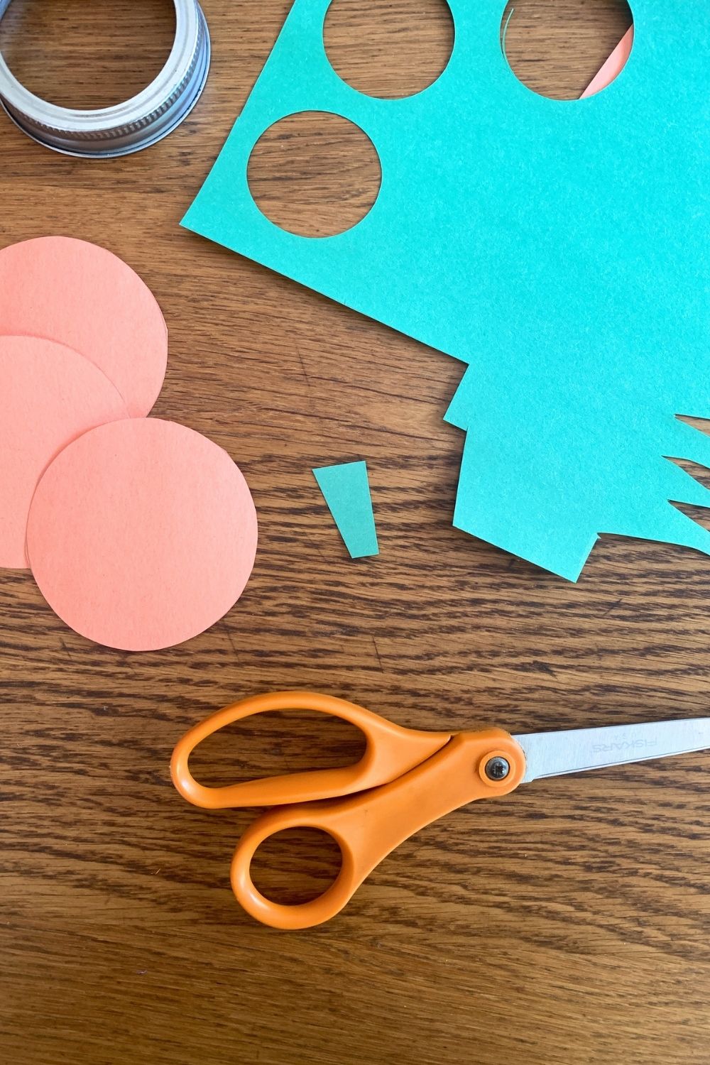 A small green paper trapezoid beside a stack of orange paper circles.