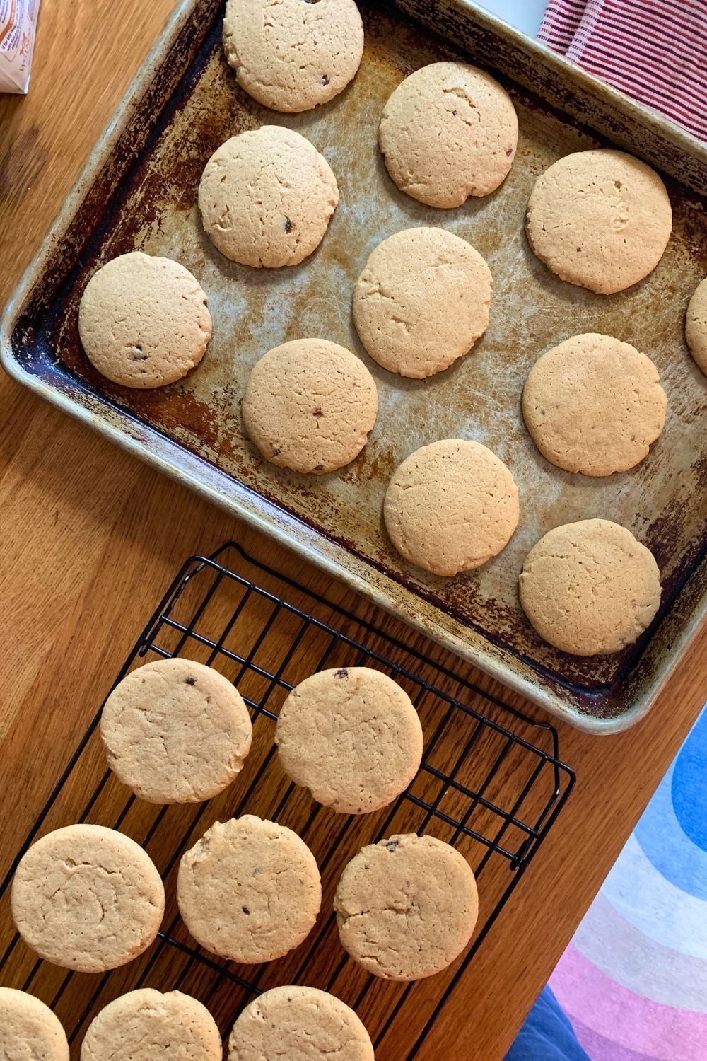 A baking sheet of cookies beside a cooling rack holding more.