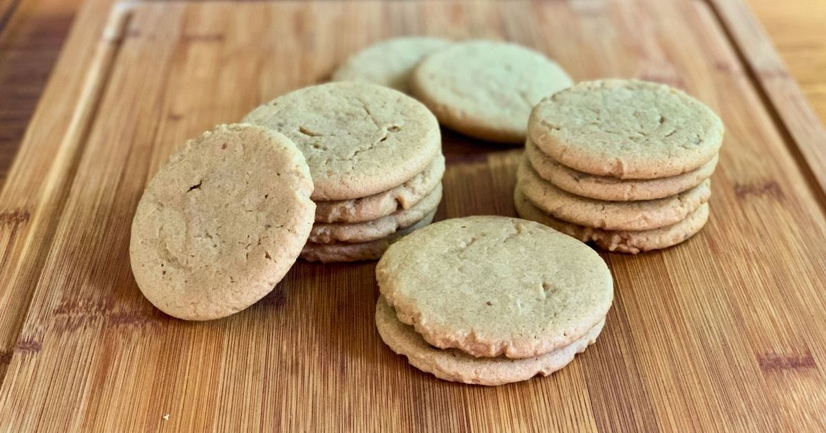 Several stacks of light brown peanut butter cookies on a wood cutting board.