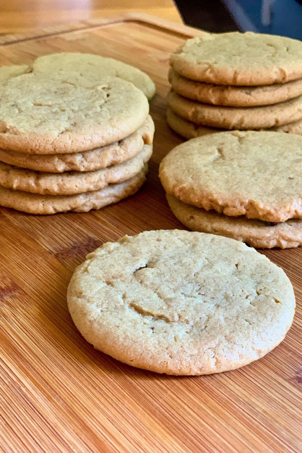 Several stacks of light brown peanut butter cookies on a wood cutting board.