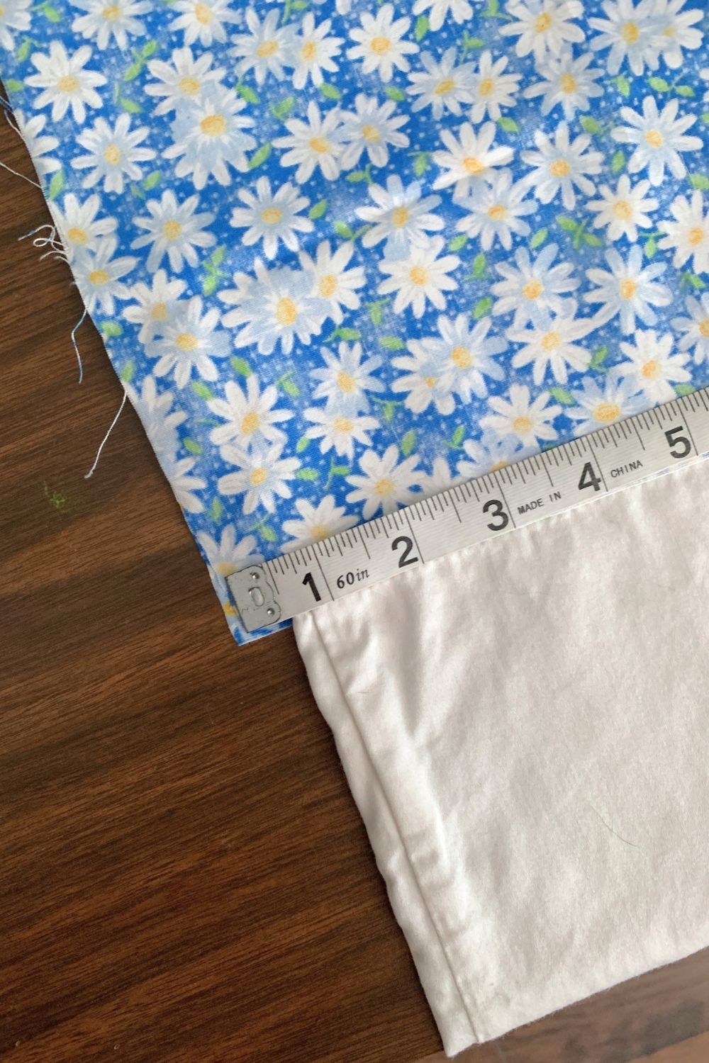 A piece of blue daisy fabric beside a white pillowcase and a fabric tape measure.