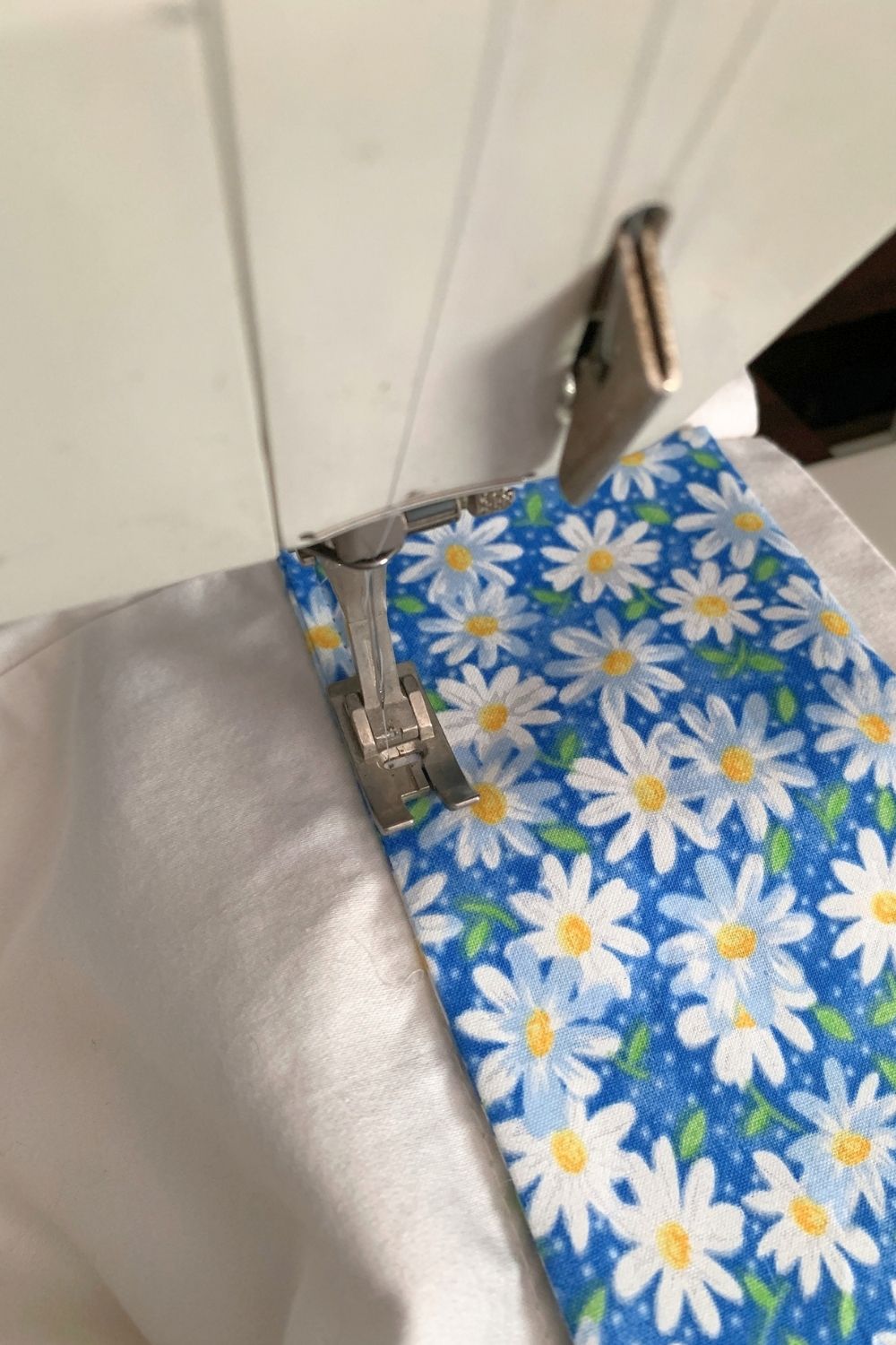 Sewing blue daisy fabric to the open end of a pillowcase.