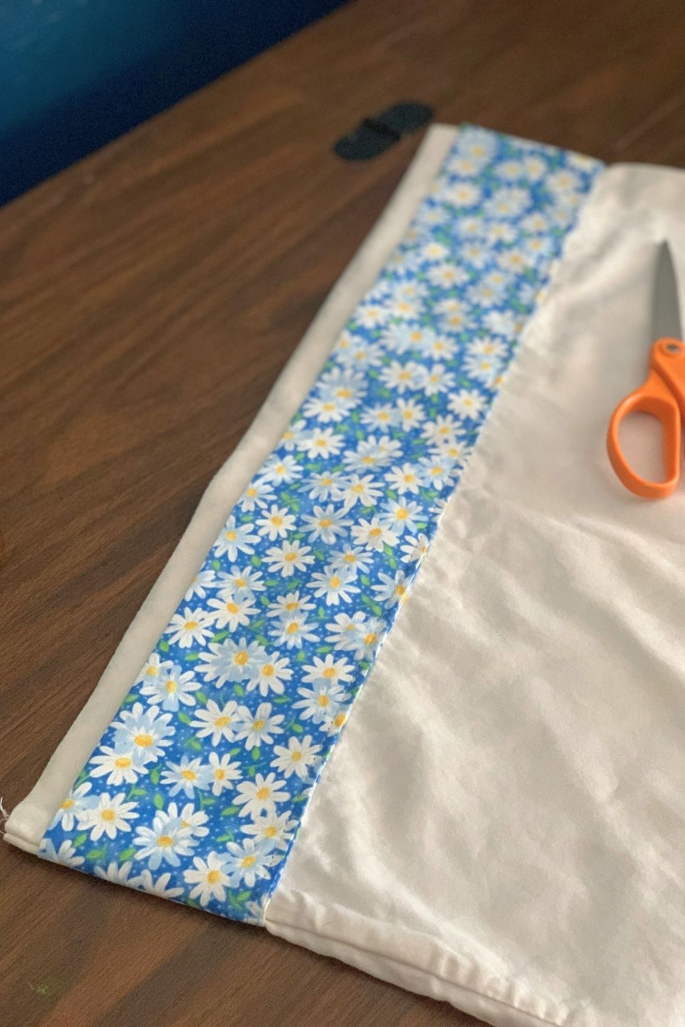 A white pillowcase with a blue daisy fabric stripe down the open side.