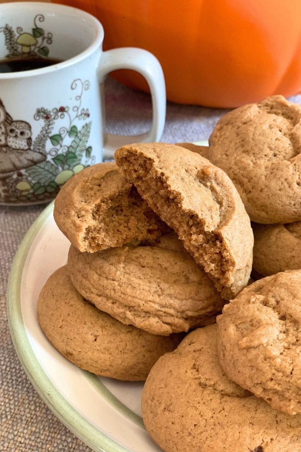 A plate of pumpkin spice sugar cookies, the top one broken in half to show the soft crumb texture.