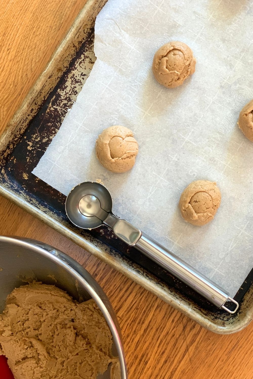 A metal cookie scoop beside a baking sheet of unbaked cookie dough portions.