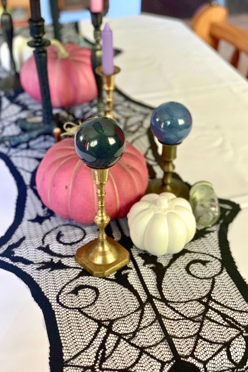 Tabletop Halloween decor with painted black and blue orbs, pink and white pumpkins, and candles.